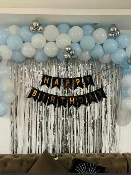 A simple and clean birthday backdrop with a blue and white balloon arch over a silver foil curtain.