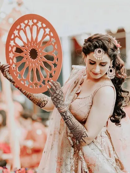A graceful photo of a bride during her mehndi ceremony. She poses with a decorative prop, her intricate henna and elegant lehenga creating a picture of traditional beauty.