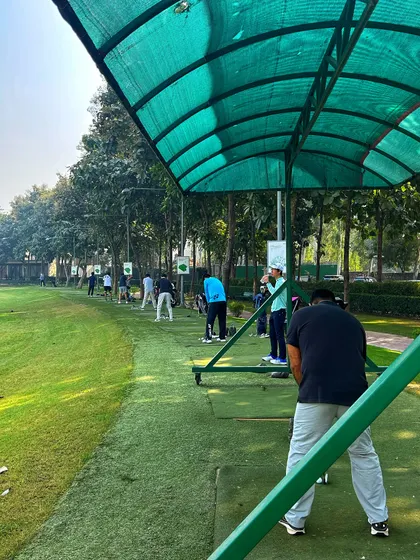 A view from under the green awning of a covered bay, looking out at a busy driving range.