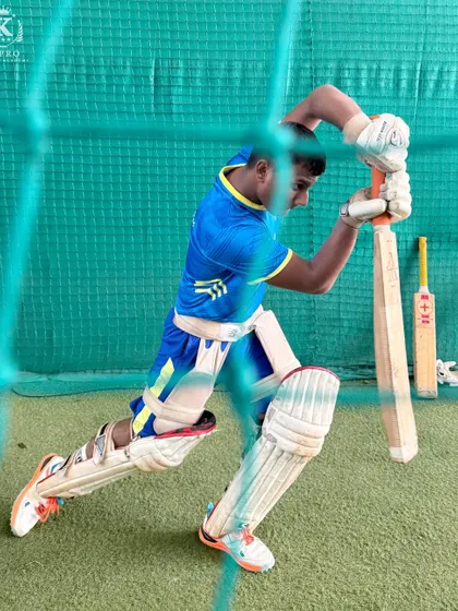 A young batsman executes a perfect front-foot defensive shot during an indoor net session, showcasing solid technique and balance.