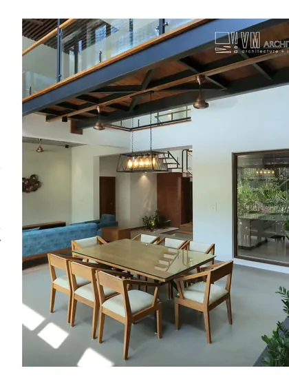 The dining area at Hamdiya House, featuring a double-height ceiling with exposed steel beams and a large window that opens to a green space.