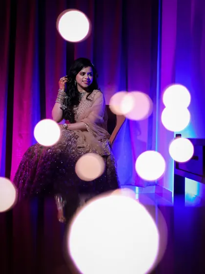 A portrait of a woman seated, with bokeh from fairy lights in the foreground, creating a magical and colorful effect.