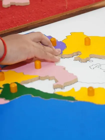A child's hand carefully places a state into the India puzzle map. This activity develops fine motor control, geographical knowledge, and an appreciation for one's own country.