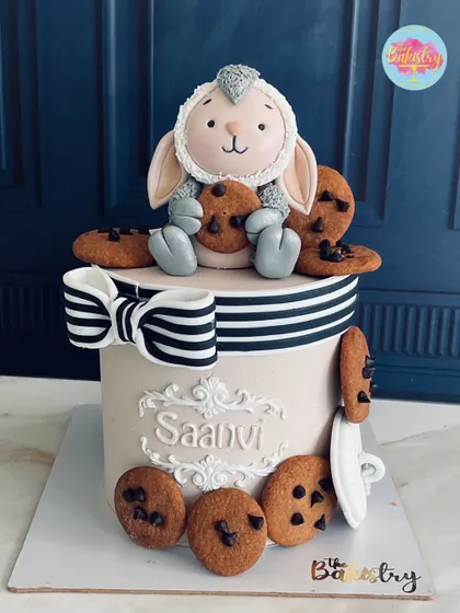 Look at this utterly charming teddy bear cake for Saanvi! The fluffy bear is hugging a cookie, surrounded by more chocolate chip cookies and a stylish striped bow.