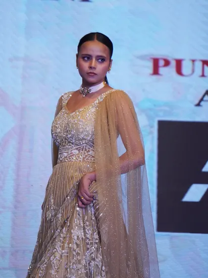 A model showcases an ornate, gold-toned lehenga, demonstrating skills in traditional Indian wear design.