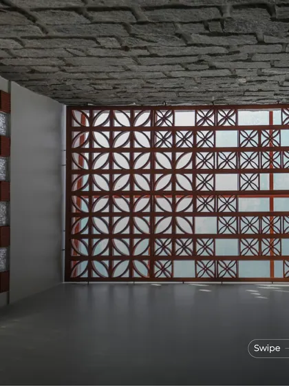 The play of sunlight through a terracotta jali screen at the Shashidhar Residence. The combination of the patterned screen, glass blocks, and stone-finished ceiling creates a rich and textured interior space.