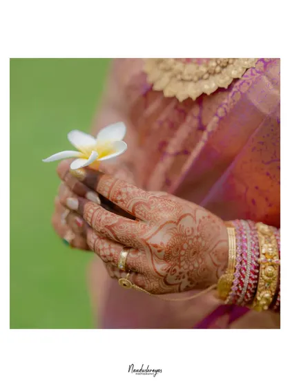 A delicate close-up of the bride's hands, adorned with intricate henna and holding a single white flower. A symbol of purity and new beginnings.