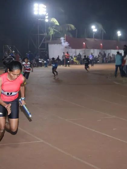 A relay runner powers through her leg of the race under the floodlights, showcasing speed and teamwork.