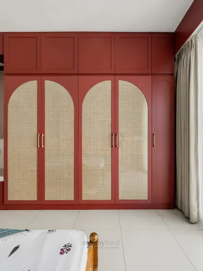 A straight-on shot of the statement wardrobe, highlighting the clean lines and the beautiful contrast between the burgundy paint and the natural cane.