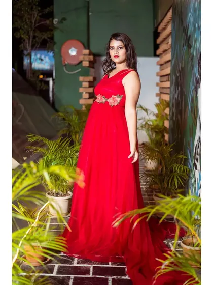 A client wearing a beautiful red tulle gown with a floral embellished belt. The dress has a long, flowing trail, perfect for creating dramatic photos.