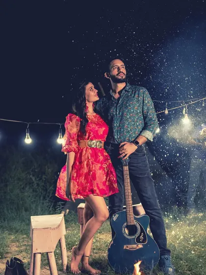 A magical night-time shot with a couple, a guitar, and a bonfire under a string of lights, creating a dreamy and musical atmosphere.