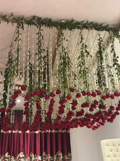 A close-up of the ceiling decoration, featuring hanging white floral strings, green vines, and a canopy of red roses.