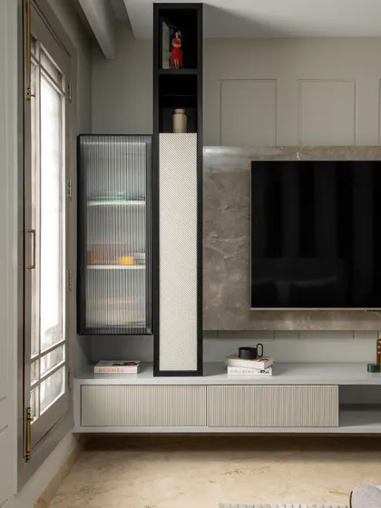 This image showcases the custom TV unit with integrated storage, including open niches and fluted glass cabinets. The design is both functional and aesthetically pleasing, maintaining the room's clean lines.