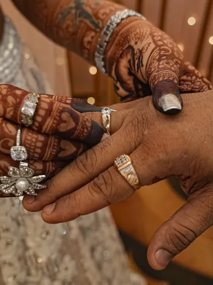 This photo captures the moment of the ring exchange. The bride's intricately designed mehendi is beautifully displayed as she places the ring on her partner's finger.