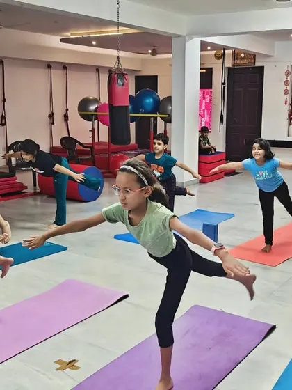This is the heart of my kids' yoga class. Here, children learn to find their balance and focus, not by being perfect, but by enjoying the process together. We work on poses like this balancing stick pose to build strength and stability in a fun group setting.