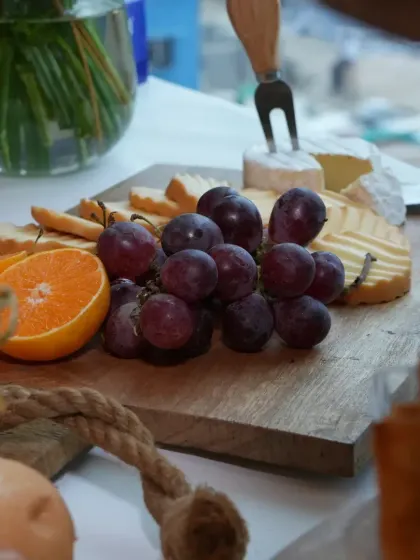 A close-up of a wooden cheese board, focusing on the fresh grapes, orange slices, and a wheel of Brie. This shot highlights the freshness and quality of the ingredients.