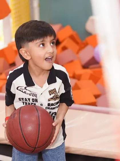A young boy looks up with excitement, ready to shoot a basket while bouncing on our trampoline.