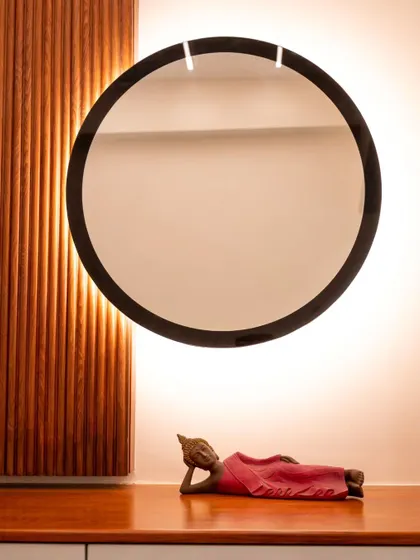 A backlit circular mirror creates a beautiful halo effect on the wall, highlighting a sleeping Buddha statue.