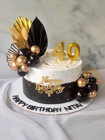 A modern and stylish cake for a 40th birthday celebration. The design features a black and white split, decorated with black and gold spheres and dried palm leaves for a contemporary look.