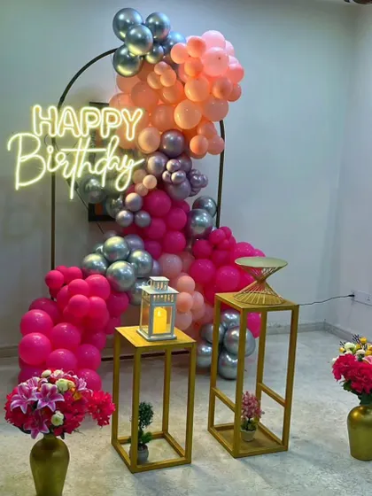 This indoor balloon arrangement uses a mix of bright pink, peach, and metallic silver balloons with a neon sign to create a vibrant and celebratory mood.