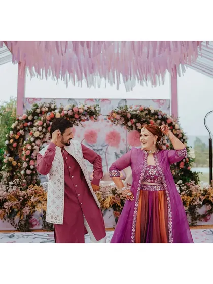 The couple shares a dance during their Mehendi ceremony, their vibrant outfits complementing the colorful floral decor.