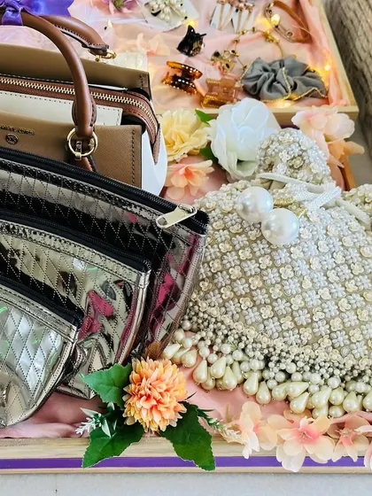 A trousseau tray dedicated to the bride's accessories. It includes a handbag, smaller pouches, and a traditional potli bag, all beautifully arranged with floral accents.