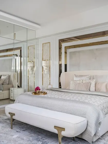 In this master bedroom, we used mirrored wardrobes to expand the sense of space. Soft curves in the furniture and layered paneling with gold accents around the bed create a plush, glamorous retreat that is a signature of our style.