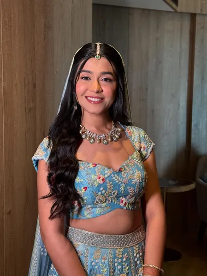 A modern and fresh half-updo with long, flowing waves. The look is completed with a delicate floral hairpiece, perfect for a daytime wedding or Mehendi.