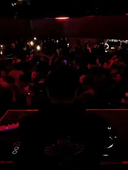 The view from the DJ booth in a dark, packed club, with the crowd silhouetted against the lights. This captures the classic nightclub atmosphere.