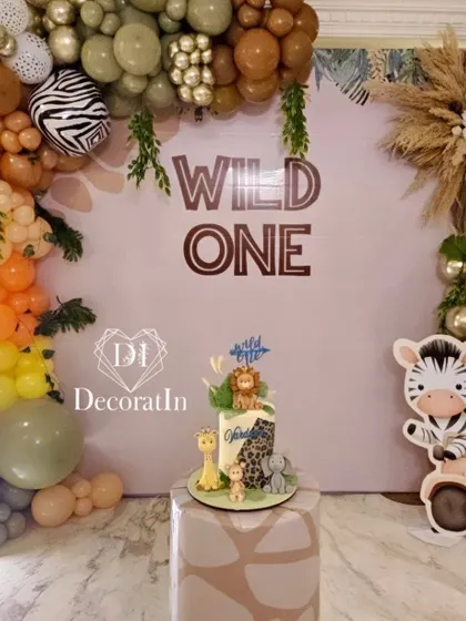 The "Wild One" jungle-themed cake-cutting area, featuring a custom backdrop, an animal-themed cake, and a vibrant balloon arch.