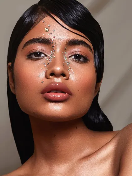 A direct and impactful beauty portrait with under-eye crystal embellishments. The focus is on the model's flawless skin and the striking, symmetrical makeup detail.