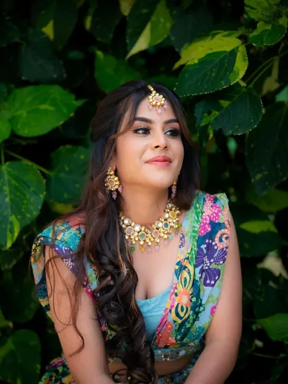 A candid, happy portrait against a dark green leafy background. The contrast makes the colors of her outfit and her bright smile pop.