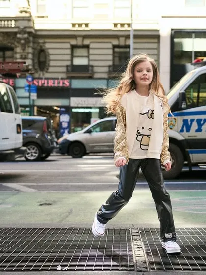 A young model confidently striding across a New York crosswalk. The NYPD van in the background grounds the image in its urban setting, adding to the cool, city-kid aesthetic.