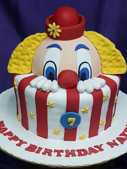 A playful clown cake for a 7th birthday. The design features a peeking clown with a red and white striped base, bringing a touch of circus fun to the celebration.