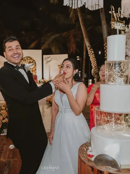 A playful cake-cutting moment. The modern, multi-tiered cake with fairy lights is a decor element in itself, set against the romantic moon-themed reception stage.