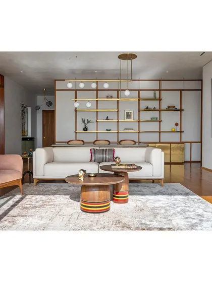 A wide view of the living room, showcasing the custom Channapatna-inspired coffee tables and the elegant, suspended shelving that acts as a subtle divider from the dining area.