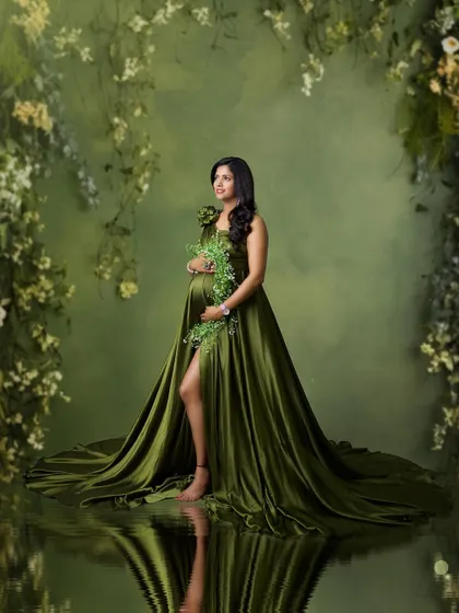 This fine art portrait that looks like a painting. The mother-to-be stands like a forest nymph in a green gown, surrounded by hanging vines and a water reflection.