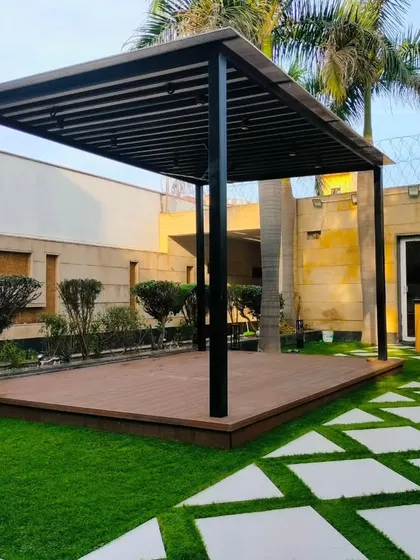 A completed landscape project in a spacious front yard in Dwarka, New Delhi. The design features a large pergola on a deck, connected by a geometric pathway.