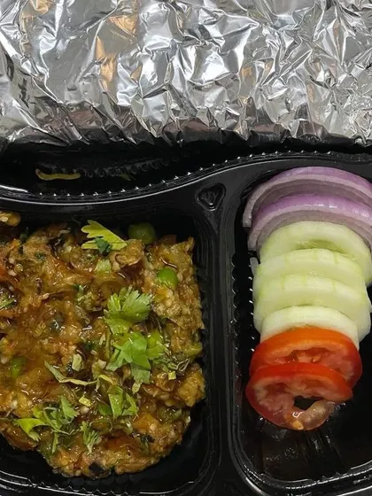 This tiffin features a home-style Baingan Bharta, a smoky roasted eggplant mash cooked with spices. It comes with fresh salad and rotis, offering a rustic and flavorful meal.
