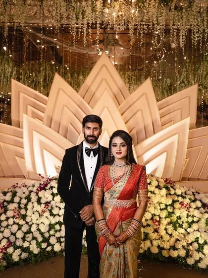 A full-length portrait of the couple standing before their magnificent floral and gold reception stage. This classic shot is a must-have for any wedding album.