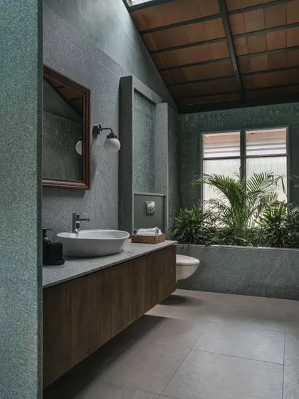 We designed this bathroom with a skylight and an indoor planter to bring nature inside. The space features grey stone-finish tiles and a floating wooden vanity, creating a spa-like, tranquil atmosphere.