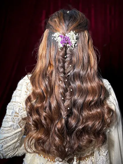 A romantic half-up hairstyle with a fishtail braid and soft waves, adorned with fresh flowers.