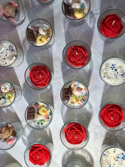 A top-down view of a diverse bulk order featuring various shot glass candle designs, including red roses and chocolate donut themes. This highlights the variety I can offer within a single large order.