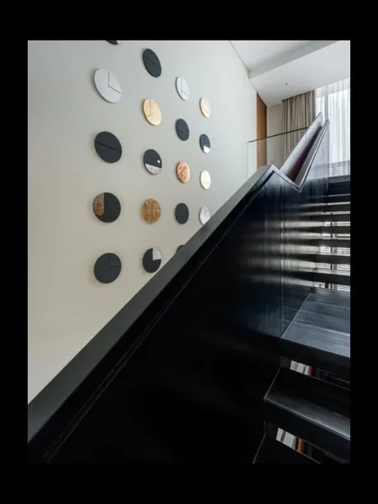 The staircase is more than a transition; it's a sculptural element. A collection of custom-made circular art pieces, finished with vegetable dyes and gold leaf, creates a dynamic installation along the wall, transforming the act of moving through the home into a visual experience.