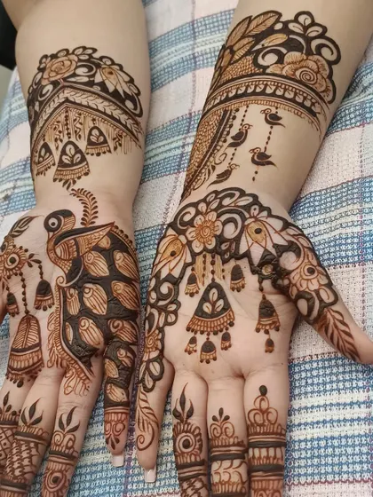 This design combines several traditional elements, including peacocks, hanging 'jhumkas' (earrings), and architectural tops. It tells a story on the hands.
