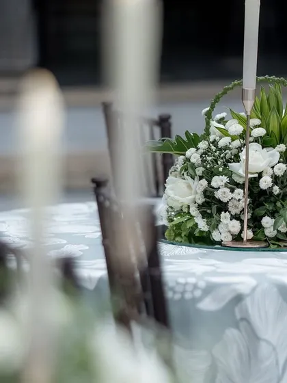 A floral centerpiece with white roses and candles on a table set for a reception, showcasing elegant table decor.