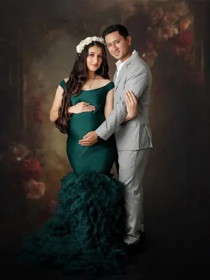 This portrait combines a dramatic, painterly backdrop with a modern mermaid-style gown. The couple's pose is classic and romantic, resulting in a truly artistic maternity photograph.