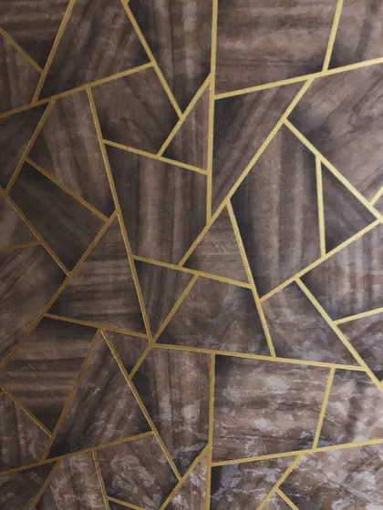 A close-up of a wallpaper with a dark wood texture and inlaid gold geometric lines. This design is a great way to get a high-end panelled look.