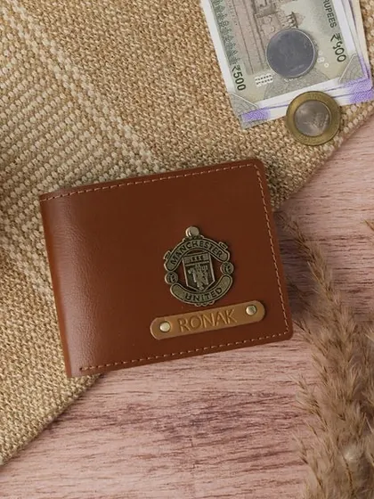 A great gift for a football fan, this personalized vegan leather wallet features the Manchester United logo charm. The name "Ronak" is embossed on a metal strip for a premium finish.