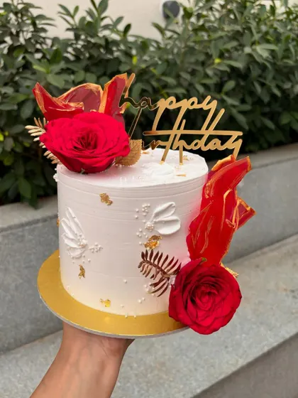 A striking white and red birthday cake. The design is decorated with fresh red roses and abstract red rice paper sails.